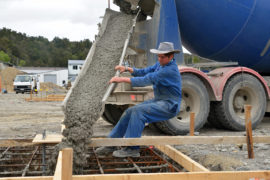 EFA7E6 A builder directs wet concrete from a cement truck into the foundations of a large building.